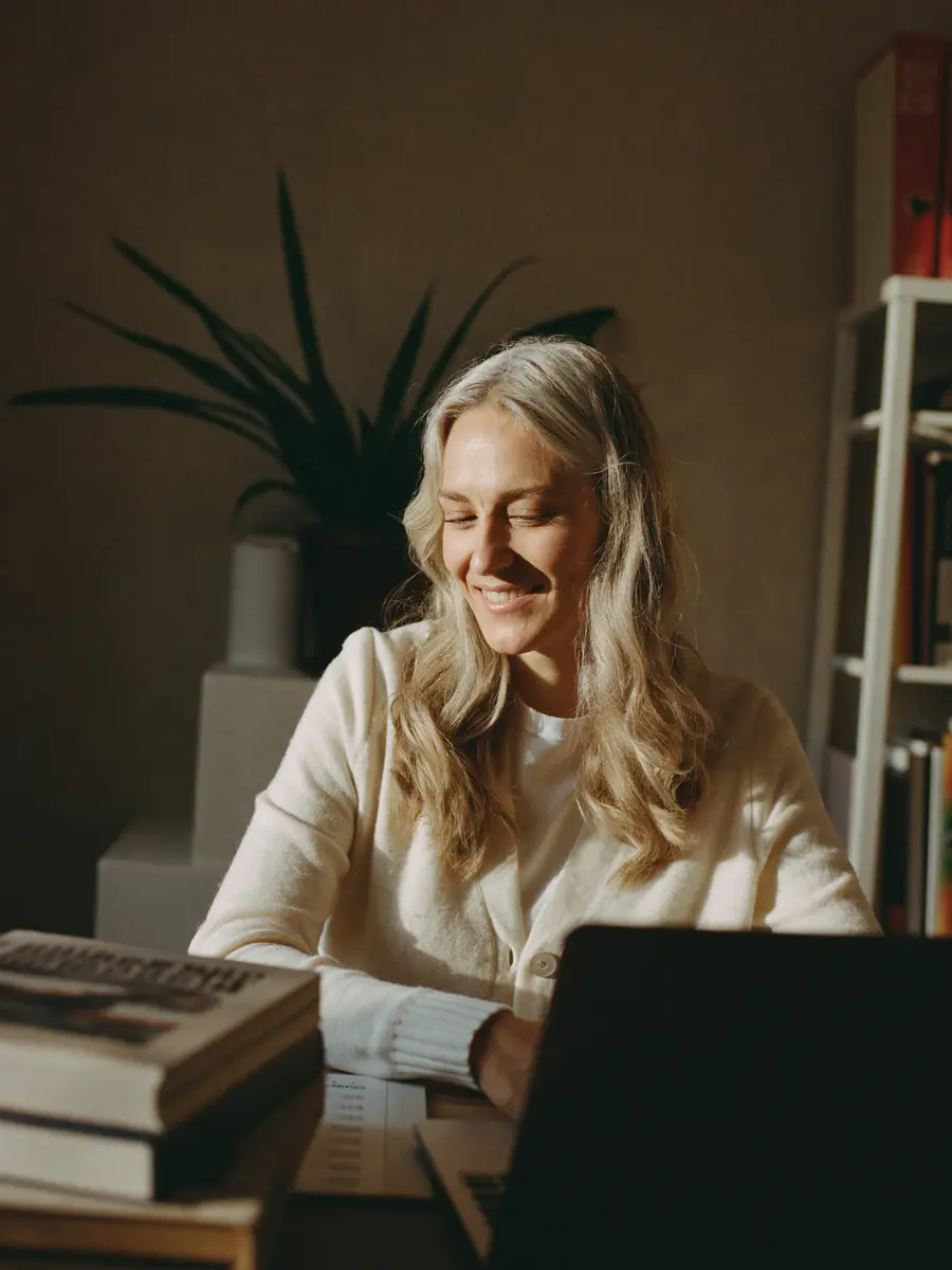 A member smiling at her laptop in a sunlit home office